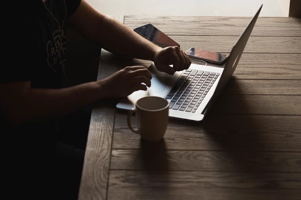 Mãos sobre o teclado de um notebook, ao lado de uma xícara de café